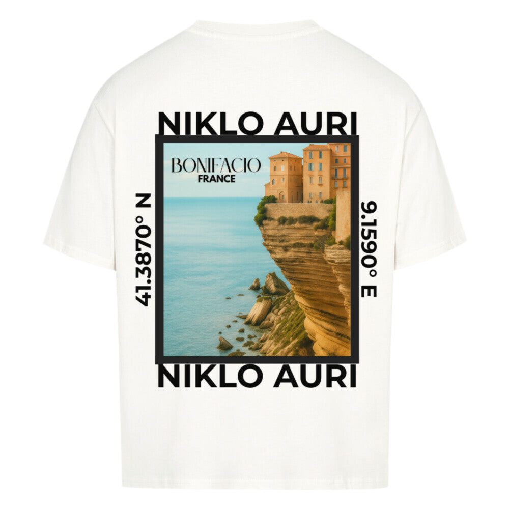 Weißes T-Shirt mit Rückendruck einer Illustration von Bonifacio, Frankreich. Zu sehen sind Häuser auf dramatisch abfallenden Felsen an der Mittelmeerküste. Der türkisfarbene Ozean erstreckt sich im Hintergrund. Oben und unten steht „NIKLO AURI“, seitlich die Koordinaten 41.3870° N und 9.1590° E. Mittig ist der Schriftzug „BONIFACIO – FRANCE“ platziert.