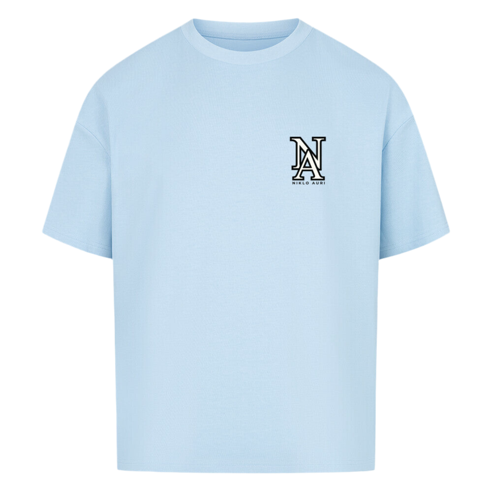 Hellblaues T-Shirt mit Rückendruck einer Illustration von Bonifacio, Frankreich. Zu sehen sind Häuser auf dramatisch abfallenden Felsen an der Mittelmeerküste. Der türkisfarbene Ozean erstreckt sich im Hintergrund. Oben und unten steht „NIKLO AURI“, seitlich die Koordinaten 41.3870° N und 9.1590° E. Mittig ist der Schriftzug „BONIFACIO – FRANCE“ platziert.